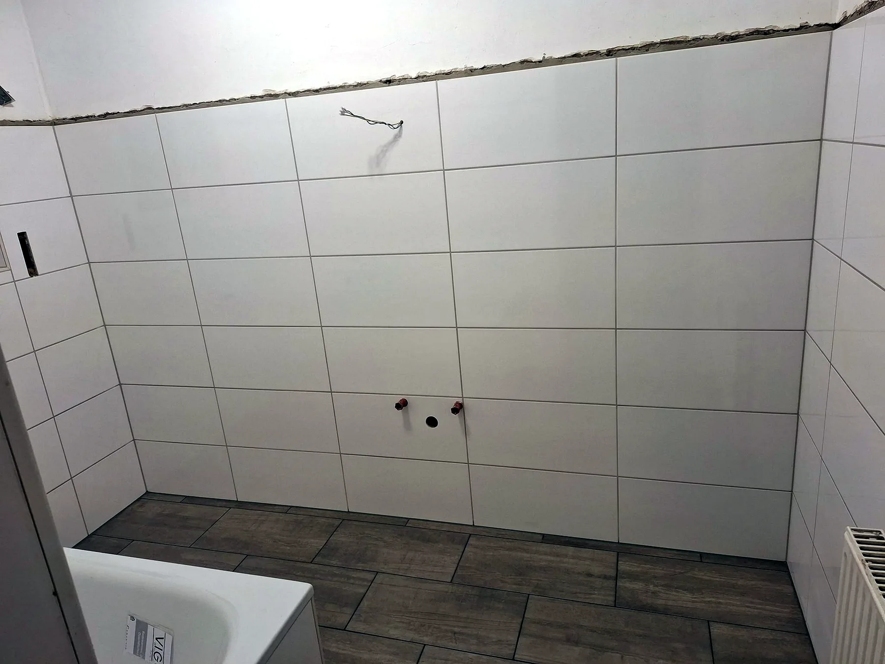 Badewanne mit weißen Wandfliesen und grauem Bodenbelag