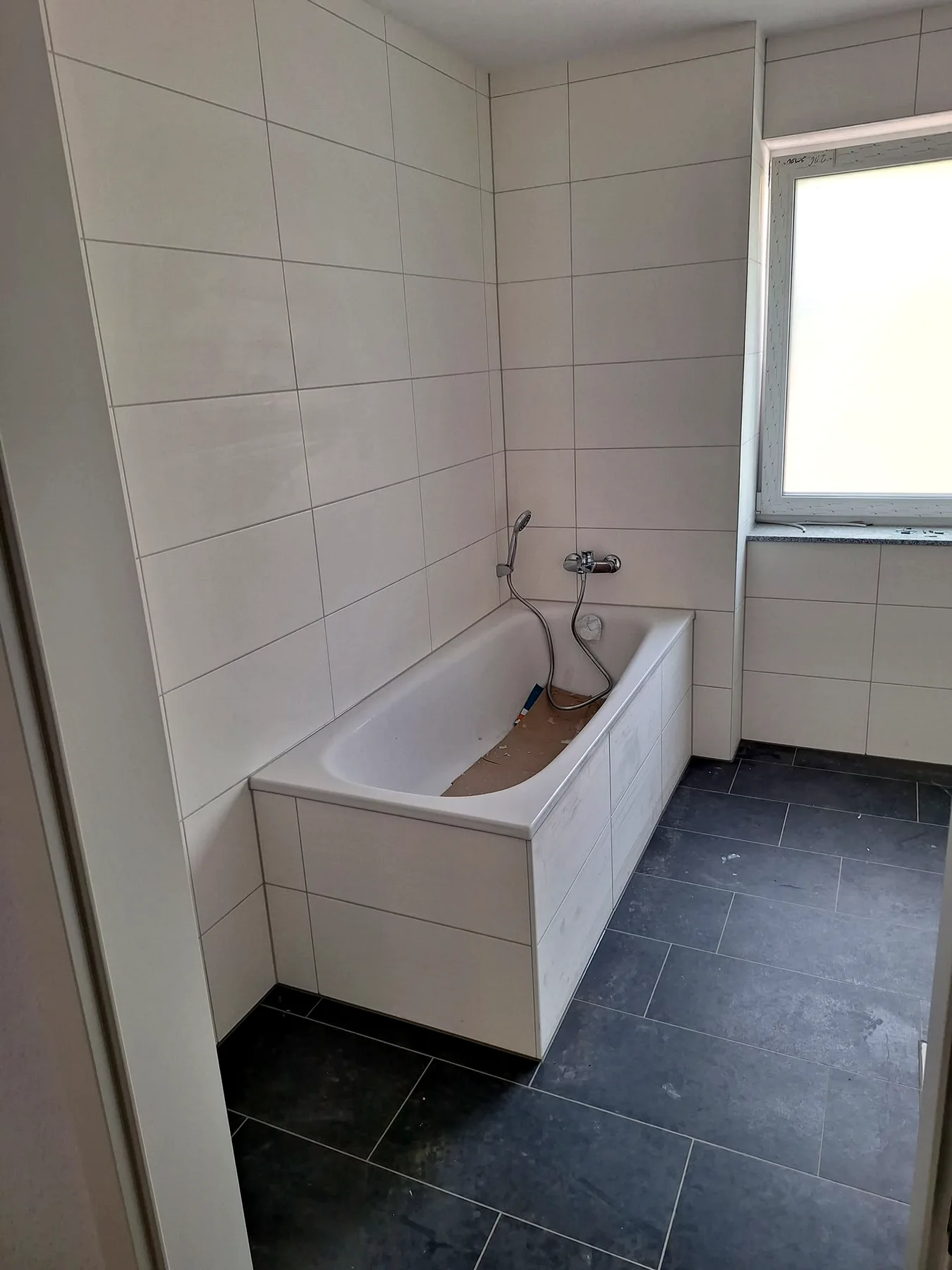 Badewanne mit weißen Wandfliesen und dunklem Fliesenboden