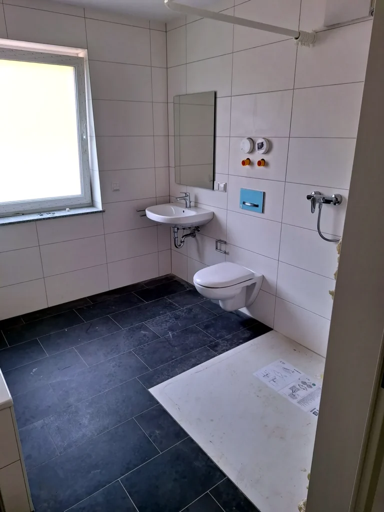 Modernisiertes Bad mit hellen Wandfliesen und dunklem Boden
